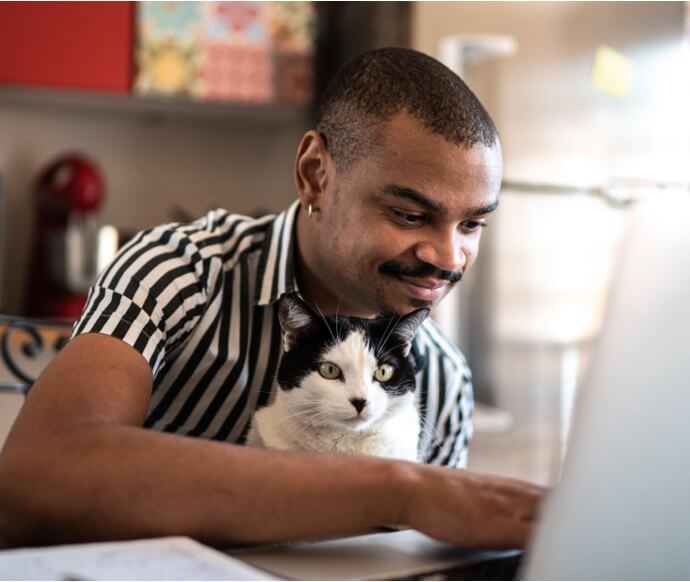 Mann am Laptop mit Katze im Arm