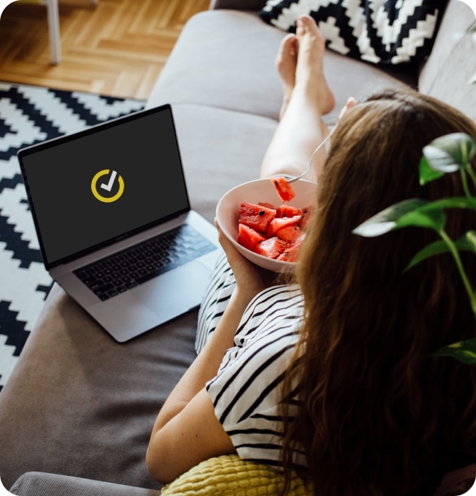 Frau auf dem Sofa mit Obstschale, neben ihr ein Laptop mit Norton-Logo