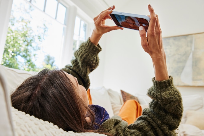 Auf dem Rücken liegende Frau schaut auf ein Mobiltelefon